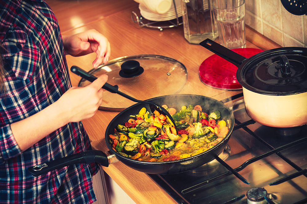 A woman is cooking vegetables in a pan